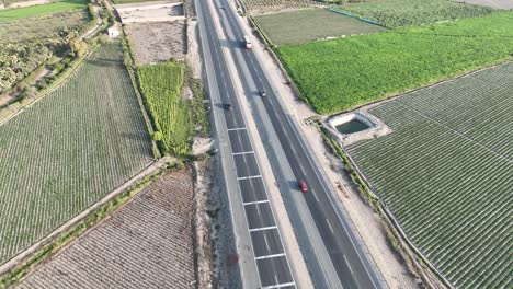 Top-Down-aerial-shot-of-vehicles-crossing-four-lane-Panamericana-Norte-highway-in-Peru-through-farming-fields-on-both-corners