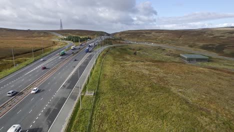 Drone-footage-showing-traffic-on-M62-at-windy-Hill-in-dappled-sunlight-at-its-highest-point-in-the-Pennine-hills,-Yorkshire-United-Kingdom