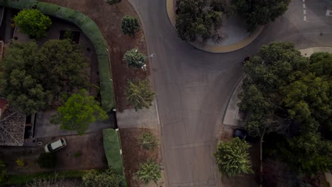 Aerial-top-down-view-of-a-motorist-making-a-traffic-circle-on-a-quiet-residential-road-at-the-side-of-a-dam