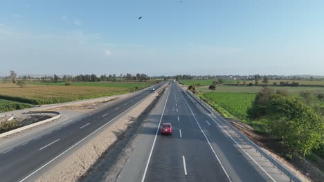 Drone-following-a-car-riding-on-a-multi-lane-road-of-Panamericana-Norte-Peruvian-highway-through-farming-fields-on-both-corners-and-birds-flying-in-the-sky