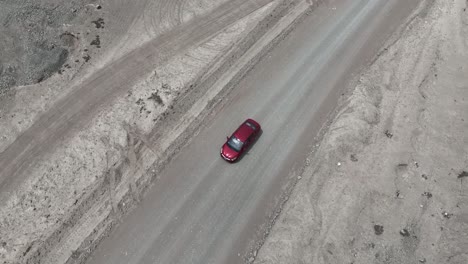 Aerial-birdseye-shot-of-a-moving-red-vehicle-in-the-desert-of-peru-on-a-dusty-desert-road-in-the-direction-of-the-holy-city-of-caral-on-a-sunny-day