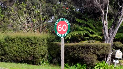 A-green-and-red-signpost-on-road-indicating-safety-zone-and-60kph-car-speed-limit,-on-popular-hiking-trail-of-New-Zealand,-Aotearoa
