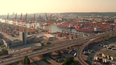 Cinematic-aerial-shot-of-industrial-harbor-and-traffic-on-road-in-Gdynia-during-golden-sunrise
