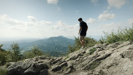 Man-in-dark-shirt-and-light-shorts,-walking-down-to-the-viewing-spot-to-see-into-the-valley-from-moutain-Donačka-gora