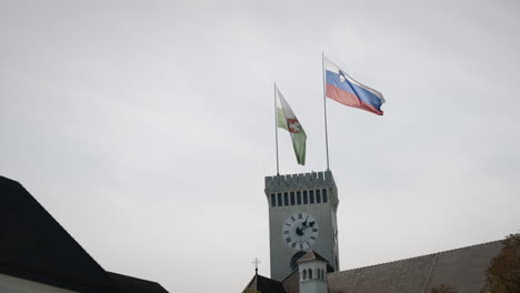 Slovenian-flag-and-flag-of-city-Ljubljana-are-held-aloft-and-flap-in-the-wind-at-the-tower-of-castle-Ljubljana-in-cloudy-weather