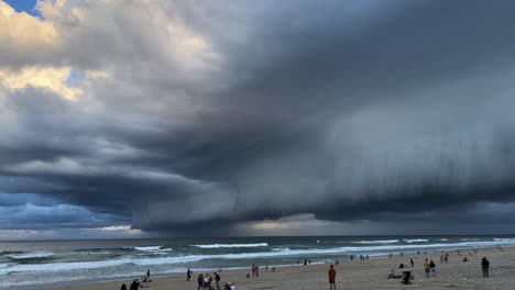 People-at-the-beach-in-surfers-paradise,-observing-the-dramatic-thick-layer-of-dark-clouds-in-the-sky,-severe-and-extreme-weather-approaching-in-storm-season-at-Gold-Coast,-Queensland,-Australia