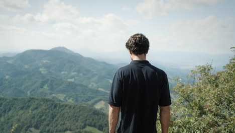 Man,-wearing-dark-shirt,-looking-ito-the-valley-from-peak-of-the-mountain