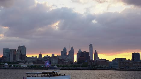 Philadelphia,-Pennsylvania---28.-August-2022:-Ein-Blick-Auf-Die-Skyline-Von-Philadelphia-Mit-Dem-Sonnenuntergang-Dahinter-Und-Dem-Fluss-Im-Vordergrund-Mit-Einem-Boot,-Das-Auf-Dem-Fluss-Fährt