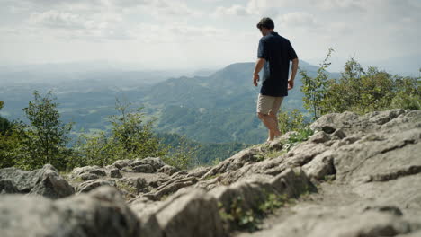 MAn-in-dark-shirt-and-light-shorts-walking-down-the-rocks-to-the-viewing-point-to-see-into-the-valley