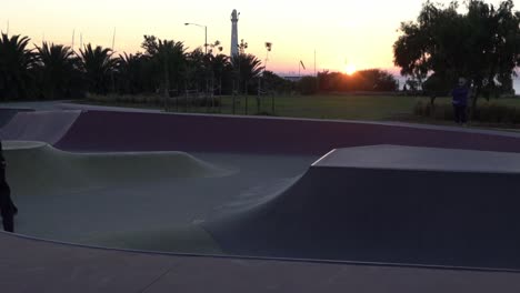 Slow-motion-shot-of-boy-grinding-on-rail-at-a-skate-park-skateboarding-during-sunset