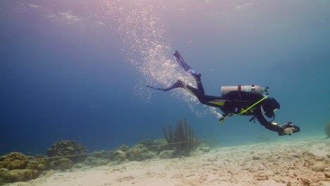 Scuba-Diver-playing-with-underwater-scooter-over-sandy-ground