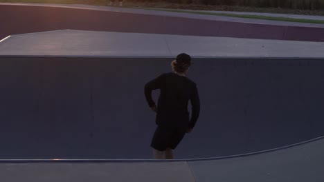 Slow-motion-shot-of-man-grinding-a-rail-at-a-skate-park-skateboarding-during-sunset