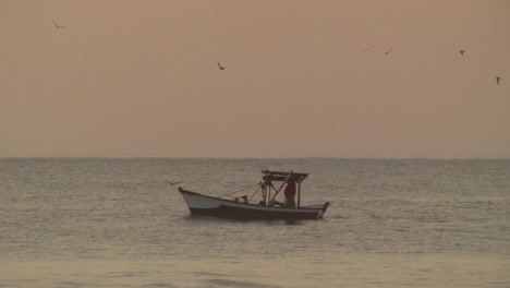 Pescador-Pescando-En-Bote-Pequeño-En-El-Mar,-Fondo-De-Cielo-Dorado,-Atardecer