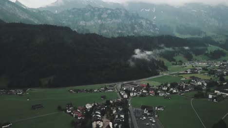 Drone-aerial-slow-pan-up-over-small-swiss-town-Endelberg-to-show-big-mountain-ranges-on-a-cloudy-day