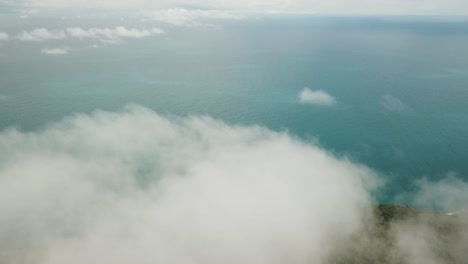 Drone-aerial-above-clouds-panning-down-to-tropical-island-with-blue-water-in-summer