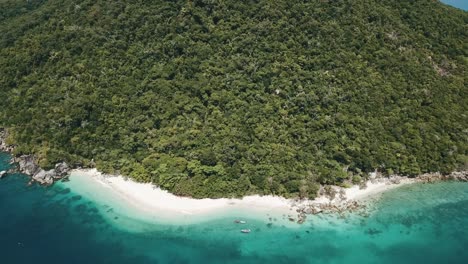 Drone-aerial-of-tropical-beach-with-clear-blue-water-on-an-island-with-trees-and-a-forest