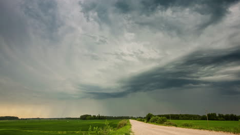 Dark-rain-clouds-over-country-road-and-green-field,-dramatic-timelapse