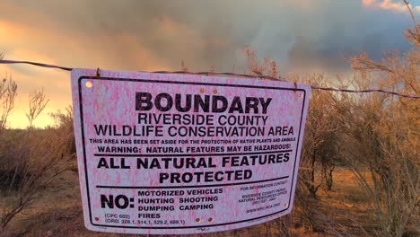 Conservation-boundary-sign-blows-in-wind-as-large-wildfire-burns-in-the-background