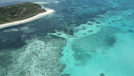 Drone-aerial-of-tropical-forest-island-pan-down-to-blue-water-water-and-reefs