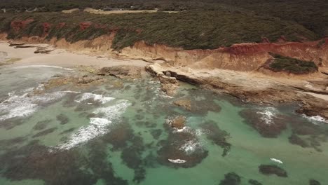 Drone-aerial-with-a-long-zoom-out-to-reveal-clear-blue-beautiful-water-and-rocky-mars-like-landscape
