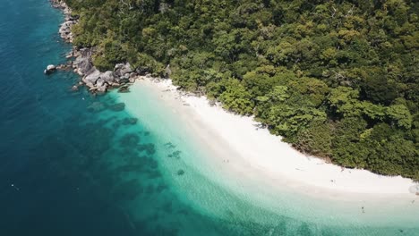 Drone-aerial-with-slow-pan-up-over-tropical-clear-blue-with-white-sandy-beach-and-tropical-forest