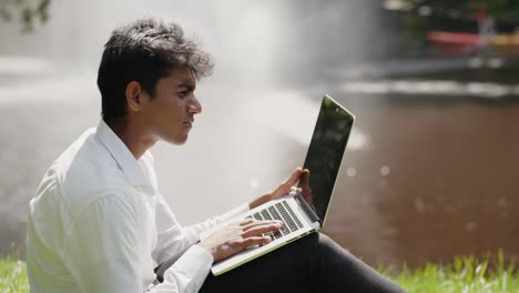 Profile-side-view-of-young-indian-man-working-outside,-confused-using-laptop