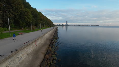 Gente-Caminando-En-El-Bulevar-En-Gdynia,-Bajo-Vuelo-De-Drones-Sobre-La-Costa,-Los-Pájaros-Comienzan-Desde-La-Costa