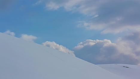 Clouds-move-over-round-snowy-hills-with-foot-tracks,-static-timelapse