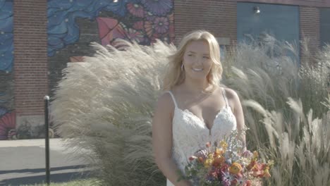 Smiling-bride-holding-a-bouquet-of-flowers-with-long-waving-plants-as-background