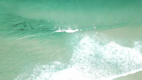 Drohnenantenne-Eines-Surfers,-Der-Eine-Welle-An-Einem-Strand-Mit-Schönem-Klarem-Blauem-Wasser-Fängt