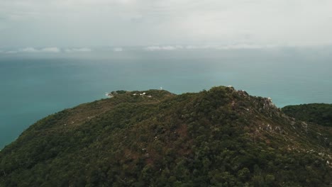 Drone-aerial-pan-up-on-tropical-island-with-blue-water-through-clouds