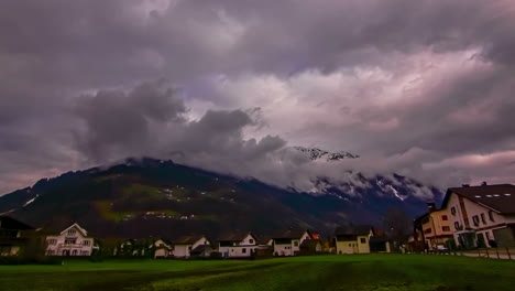 Timelapse-shot-of-dark-clouds-over-houses-on-the-foothills-of-mountain-range-during-evening-time