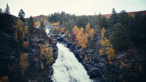 Waterfall-Flowing-In-The-Rocky-Cliff-With-Yellow-Trees-During-Autumn-In-Dovrefjell,-Norway