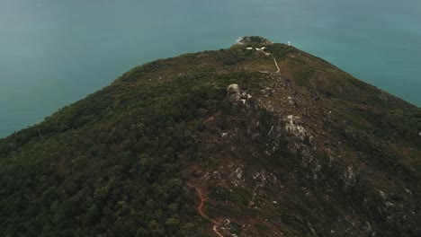 Drone-aerial-rise-and-pan-down-over-tropical-forest-island-with-hike-trail-on-a-sunny-summer-day