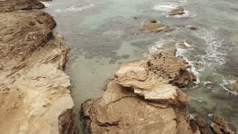 Drone-aerial-rise-and-pan-down-to-a-rocky-landscape-with-waves-crashing-onto-the-face
