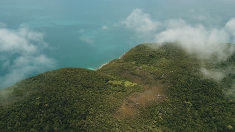 Drone-aerial-above-clouds-showing-tropical-forest-on-an-island-with-blue-water
