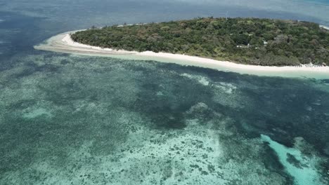 Drone-aerial-of-blue-water-water-and-reefs-pan-up-to-tropical-forest-island