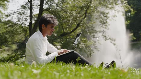 Enthusiastic-young-man-working-remotely-with-laptop-at-park,-sunny-day