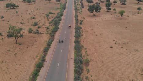 Drone-Toma-Una-Foto-Aérea-De-Los-Dos-Motociclistas-Conduciendo-Su-Bicicleta-En-La-Carretera-De-Tharparkar-Cerca-De-Sindh-Y-Pasando-Por-Un-Rickshaw
