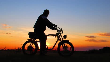 Silhouette-of-man-on-a-motorcycle,-standing-and-watching-the-sunset