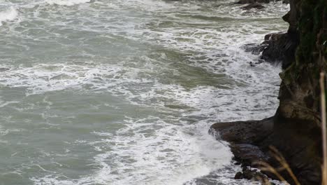 Waves-crashing-onto-high-dark-cliffs-during-seabird's-mating-season-in-Muriwai,-New-Zealand