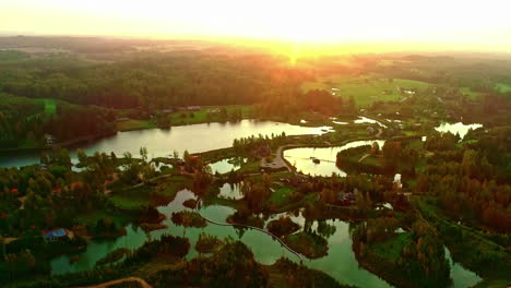 Wide-slow-forward-aerial-of-lakes-and-green-forest-landscape-by-sunset