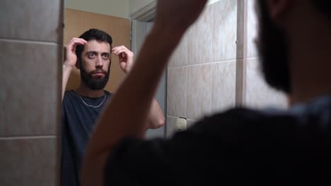 Young-Bearded-Man-Fixing-His-Hair-In-Front-Of-Mirror-Inside-The-Bathroom