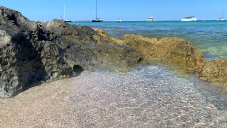 Sommertraumurlaubsziel-Auf-Der-Insel-Formentera-Ses-Illetes-Beach-Ibiza-Spanien,-Transparentes-Türkisfarbenes-Wasser-Und-Luxusyachten-Im-Urlaub,-Wellen,-Die-Auf-Felsen-Schlagen,-4k-aufnahme