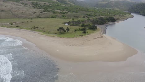 Aerial-of-Ocean-separating-with-sand-exposed-in-middle,-Transkei-rolling-hills-in-background