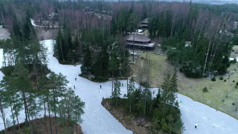 Aerial-view-of-People-having-fun-skiing-on-a-frozen-lake-surrounded-by-tall-trees,-Nordic-outdoor-activities