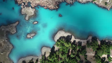 Cinematic-drone-shot-of-turquoise-colored-water-in-the-mountains-at-Naltar-Valley-in-Pakistan,-slowly-descending-and-rotating-aerial-shot