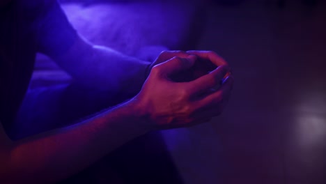 Static-shot-of-a-man-tapping-his-fingers-together-surrounded-by-smoke-in-vibrant-lighting