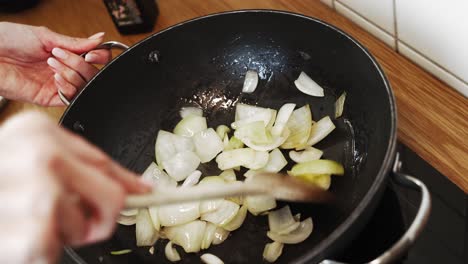 Woman's-hands-stirfrying-onion-on-a-frypan-in-slow-motion