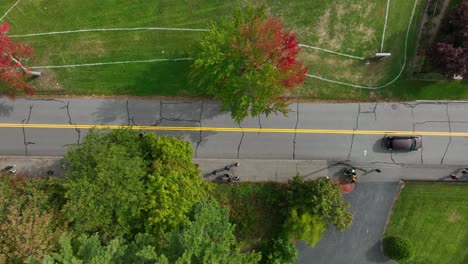Straight-down-aerial-shot-of-sedan-cars-driving-down-street-and-coming-to-stop-at-intersection-where-pedestrians-cross-crosswalk